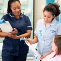 A senior nurse overseeing a student as she discusses a document with a patient.