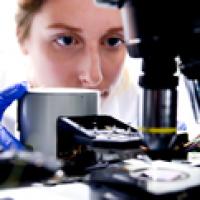 A female student closely studying an optoelectronic device beneath a microscope