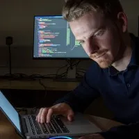 cyber security student looking at their computer in a dark room