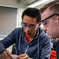 Two male undergraduate electronic engineering students with goggles adjusting device