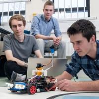 Three male wireless communications engineering students testing a robot