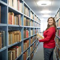 A student smiling over her shoulder as she carries a pile of books through the stacks in Hartley library.
