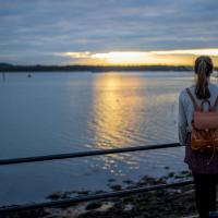 A student gazing reflectively over Southampton docks as the sun sets over the horizon in the distance.