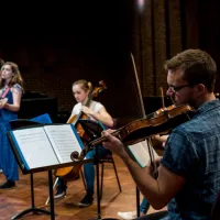 A violinist in foreground with musicians behind performing in Turner Sims