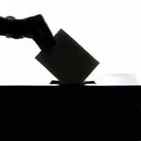 A silhouette of a hand depositing the holder's vote into a ballot box.