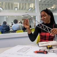 Civil engineering student Virtue Igbokwuwe, a young Black woman, works on a design at a desk in our campus building, immersed in her work