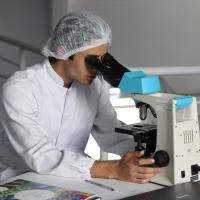 A researcher in a white lab coat looks through a microscope.