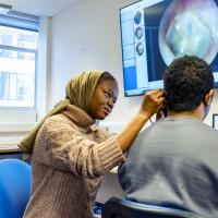 Audiology student looking into a persons ear and showing it on a big screen