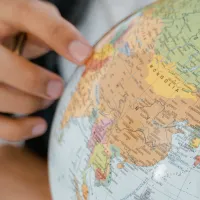 The hand of a young person points to a country on a globe model