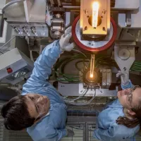 View from above of two researchers feeding glass into a fibre drawing furnace.