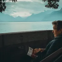 Elderly man sat on a bench next to an alpine lake