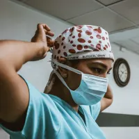 a medical practitioner adjusts their surgical cap, looking intently ahead..