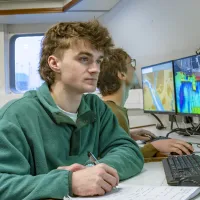 Students on the research vessel looking at screens showing colour-coded visual data of seabed mapping.