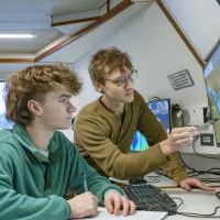 Students on the research vessel discussing screens showing colour-coded visual data of seabed mapping.