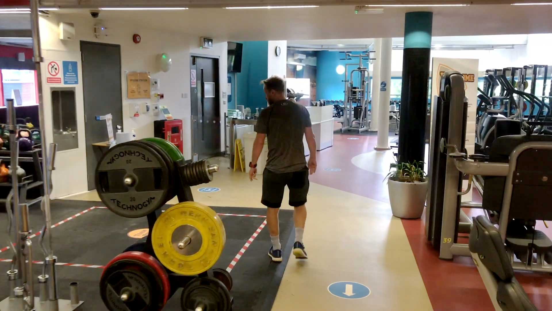 Man walking through empty gym, inspecting weights and equipment.