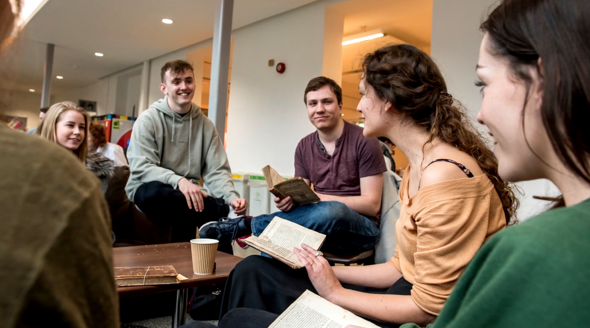 Several students gathered around a café table at Avenue Campus, discussing a book they are all reading.